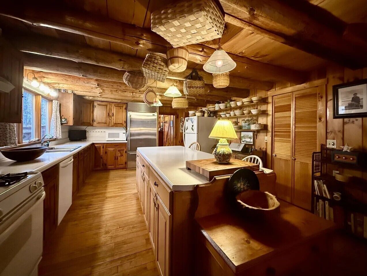 A rustic kitchen with wooden cabinets, a large island, and hanging baskets.