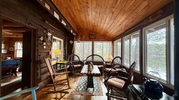 L’intérieur d’une cabane en rondins comprend un coin repas avec des meubles en bois et une grande fenêtre donnant sur une zone boisée.