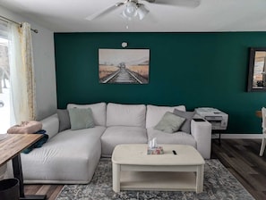 Ein Wohnzimmer mit grüner Wand, einem weißen Sofa, einem kleinen Couchtisch und einem Deckenventilator.