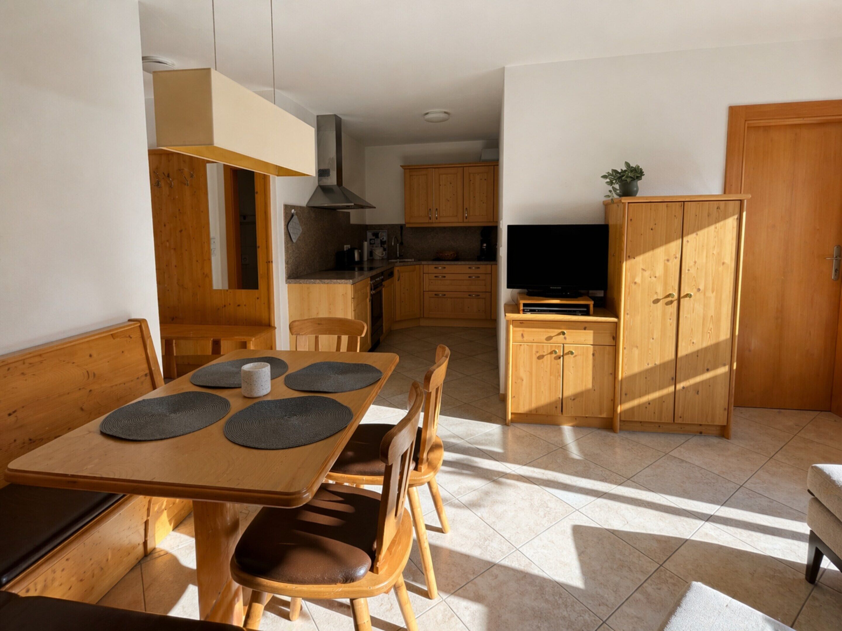 A dining area with a table, chairs, and a television in a kitchen area with wooden cabinets and a tiled floor.