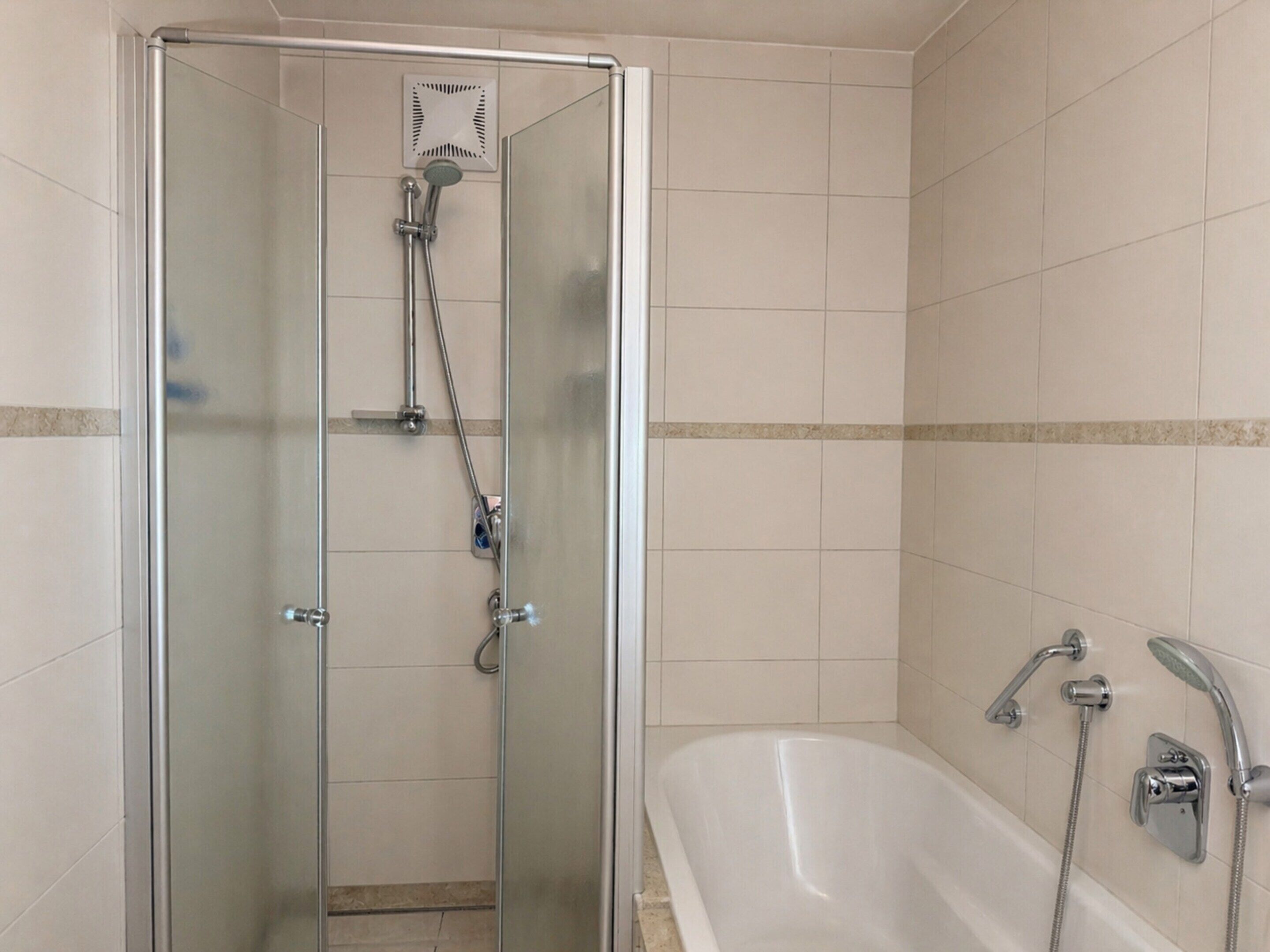 Uma casa de banho com cabine de chuveiro em vidro, banheira com duas cabeças de duche e paredes em azulejo.
