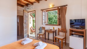 Une chambre à coucher comprenant un lit, une télévision, un petit réfrigérateur, une table avec des chaises et une fenêtre avec des rideaux.