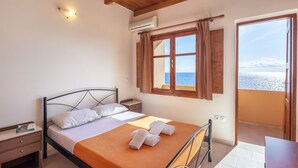 Een slaapkamer met een bed, nachtkastje, raam met gordijnen en uitzicht op zee.
