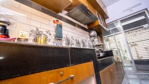A modern kitchen with a black countertop, wooden cabinets, and a tiled backsplash. - Spacious 3BR Apartment in Dhanmondi (Dhaka)