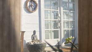 A serene outdoor area with a Buddha statue on a stone platform, a decorative wreath, and a door with glass panels. - Charming 1-bedroom cottage in Stinson Beach - walk everywhere! (Stinson Beach)