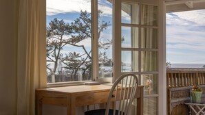 A wooden desk with a chair in front of a large window overlooking trees and a view of the sea. - Charming 1-bedroom cottage in Stinson Beach - walk everywhere! (Stinson Beach)