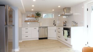 A modern kitchen with white cabinetry, a stainless steel refrigerator, a dishwasher, and an oven. There is a window above the sink and a plant hanging on the wall. - Lovely 2-bedroom in a walkable Portland neighborhood - perfect for your stay! (Portland)
