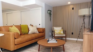 A modern living room with a brown leather sofa, a wooden coffee table, and a striped wall. - Lovely 2-bedroom in a walkable Portland neighborhood - perfect for your stay! (Portland)