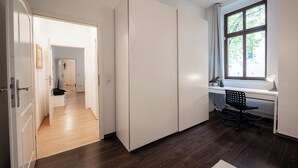 Ein modernes Zimmer mit großem Kleiderschrank, Schreibtisch mit Stuhl und Fenster mit Blick auf Bäume.