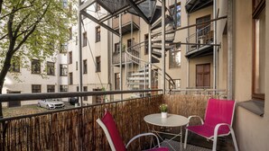 Ein Balkon mit zwei roten Stühlen, einem kleinen runden Tisch und einem geparkten Auto davor.