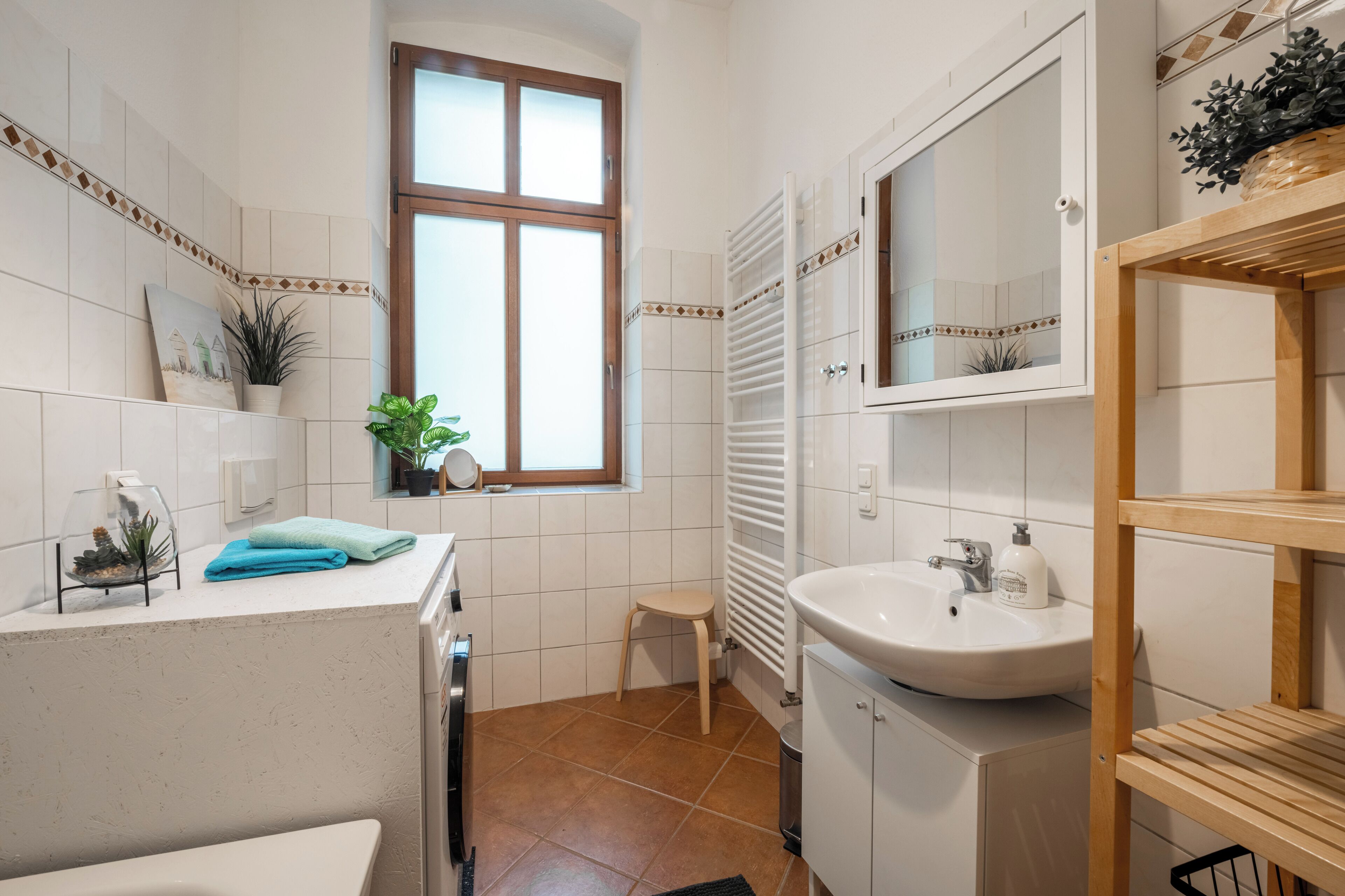 Une salle de bain avec un lavabo blanc, un miroir, une fenêtre et un porte-serviettes.