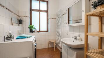 Une salle de bain avec un lavabo blanc, un miroir, une fenêtre et un porte-serviettes.