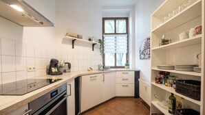 Eine kleine Küche mit weißen Schränken, einem Einbauofen und einem Fenster mit Jalousien.