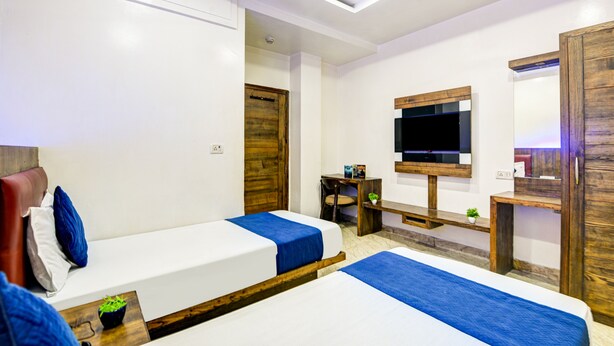 A hotel room with two single beds, a wooden wardrobe, a TV mounted on the wall, and a small table with a plant. - Hotel Saffron Inn (New Delhi)