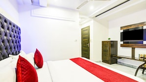 A modern hotel room with a large bed, a flat-screen TV, a wooden wardrobe, and a ceiling fan. - Hotel Saffron Inn (New Delhi)