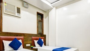 A hotel room with two beds, a ceiling fan, an air conditioning unit, and a small potted plant. - Hotel Saffron Inn (New Delhi)