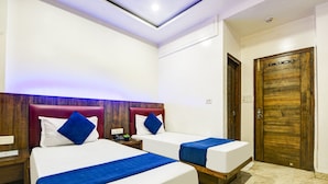 A hotel room with two beds, a wooden door, and a modern ceiling design. - Hotel Saffron Inn (New Delhi)