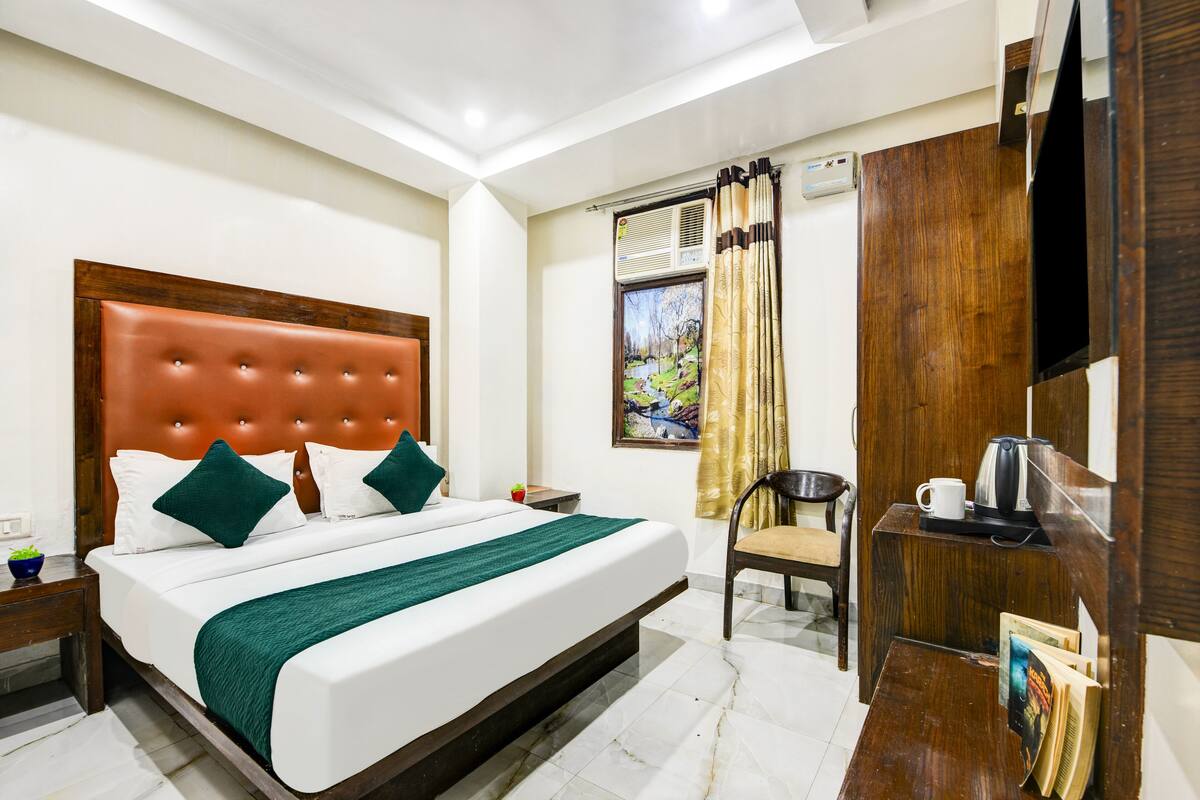 A hotel room with a large bed, a wooden headboard, a desk with a kettle, and a chair.