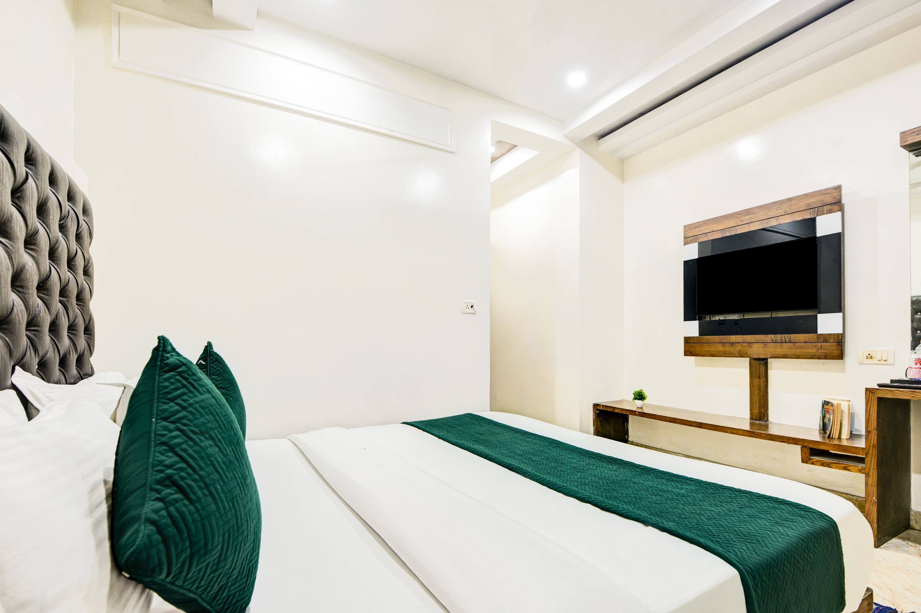 Een moderne slaapkamer met een groot bed, een flatscreen televisie aan de muur en een houten nachtkastje.