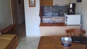 Kompakti keittiö, jossa on mikroaaltouuni, kahvinkeitin ja pieni ruokailutila, jossa on pöytä ja tuolit.