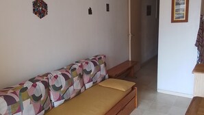 Huoneessa on puinen vuodesohva, pieni pöytä ja ovi, joka johtaa toiseen huoneeseen.