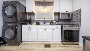 Cocina compacta con armarios blancos, microondas integrado, horno de acero inoxidable y lavadora.