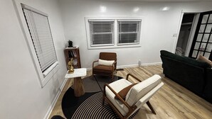 Una sala de estar con piso de madera, un sofá de cuero marrón, un sillón blanco, una mesita auxiliar y una estanterÃa.