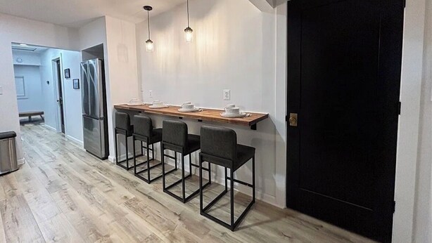 Una cocina moderna con una mesa de madera y cuatro sillas, un refrigerador y lámparas colgantes.