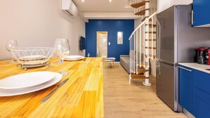 Une cuisine moderne avec une table à manger en bois pour deux personnes, un réfrigérateur en acier inoxydable et un mur d’accent bleu.