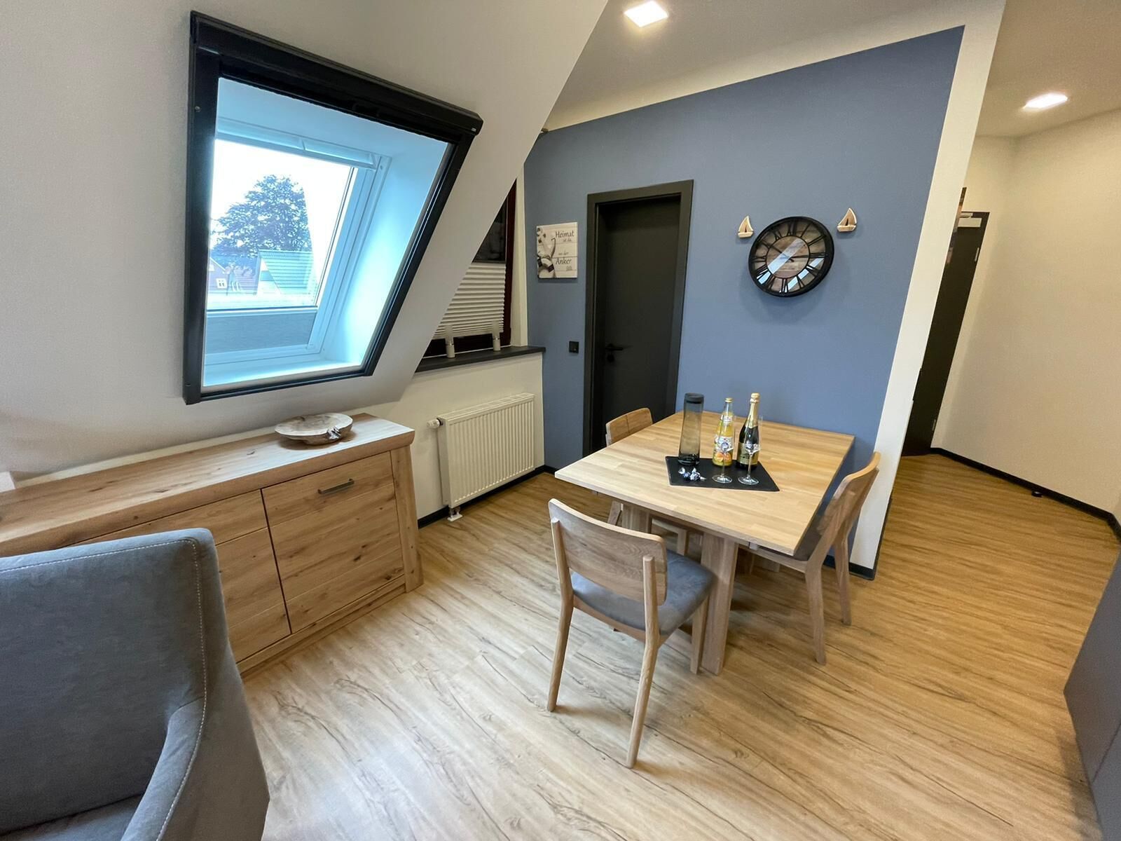 Eine moderne Küche mit Oberlicht, einem Essbereich mit Holztisch und Stühlen sowie einer Uhr an der Wand.