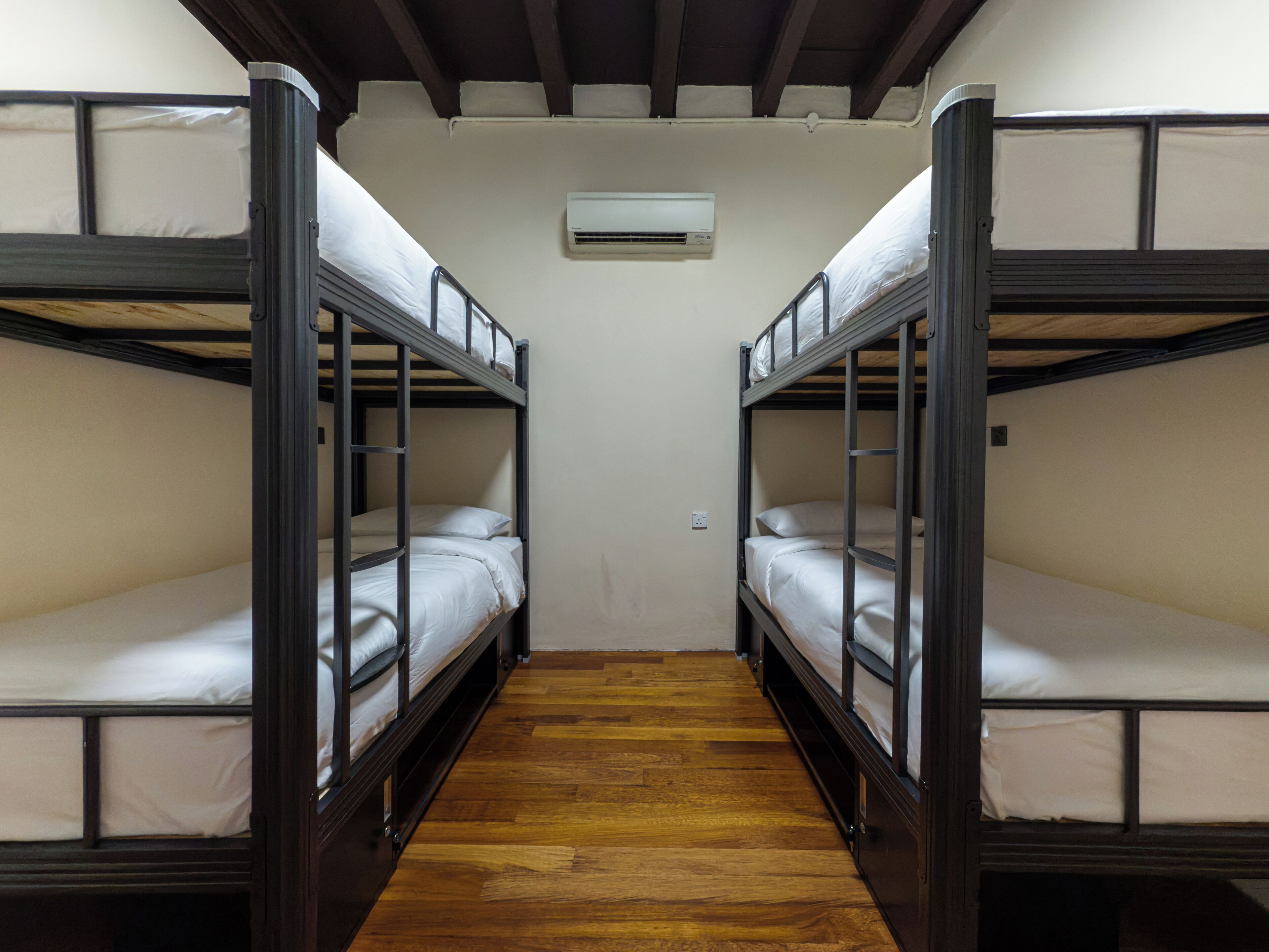 A room with bunk beds, wooden flooring, and an air conditioning unit on the wall.