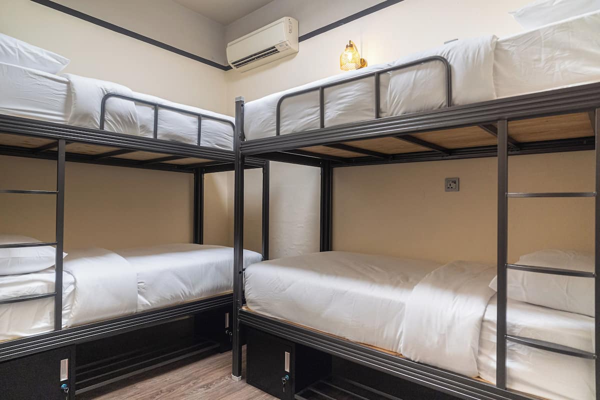A bunk bed room with two beds, a wall-mounted air conditioner, and a small wall-mounted light fixture.