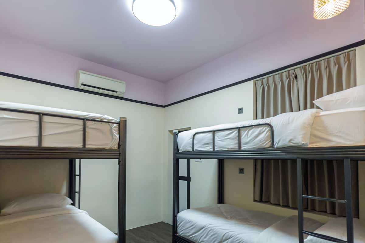 A dormitory room with bunk beds, a ceiling light, an air conditioning unit, and a window with curtains.