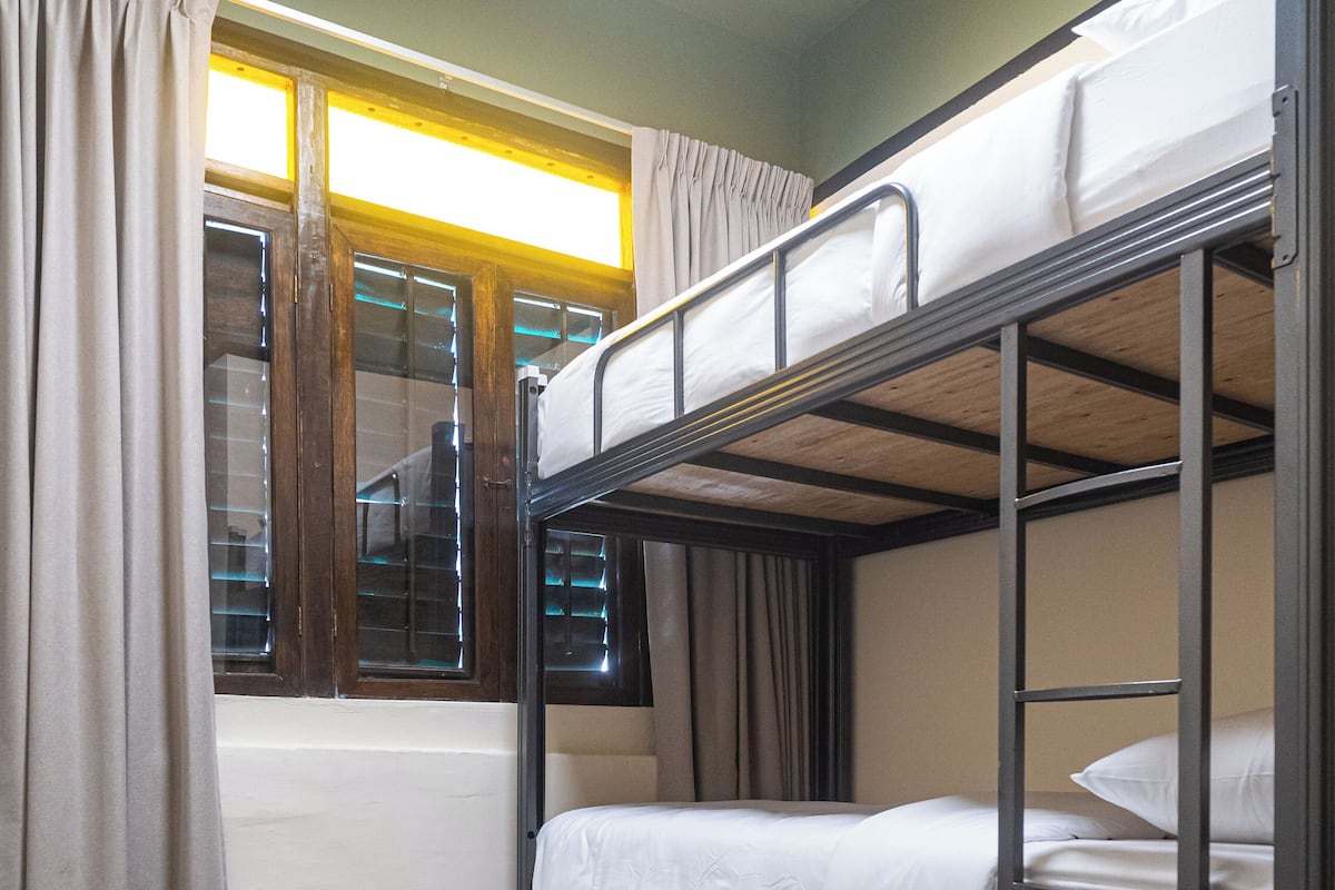 A bunk bed room with a window, curtains, and wooden flooring.