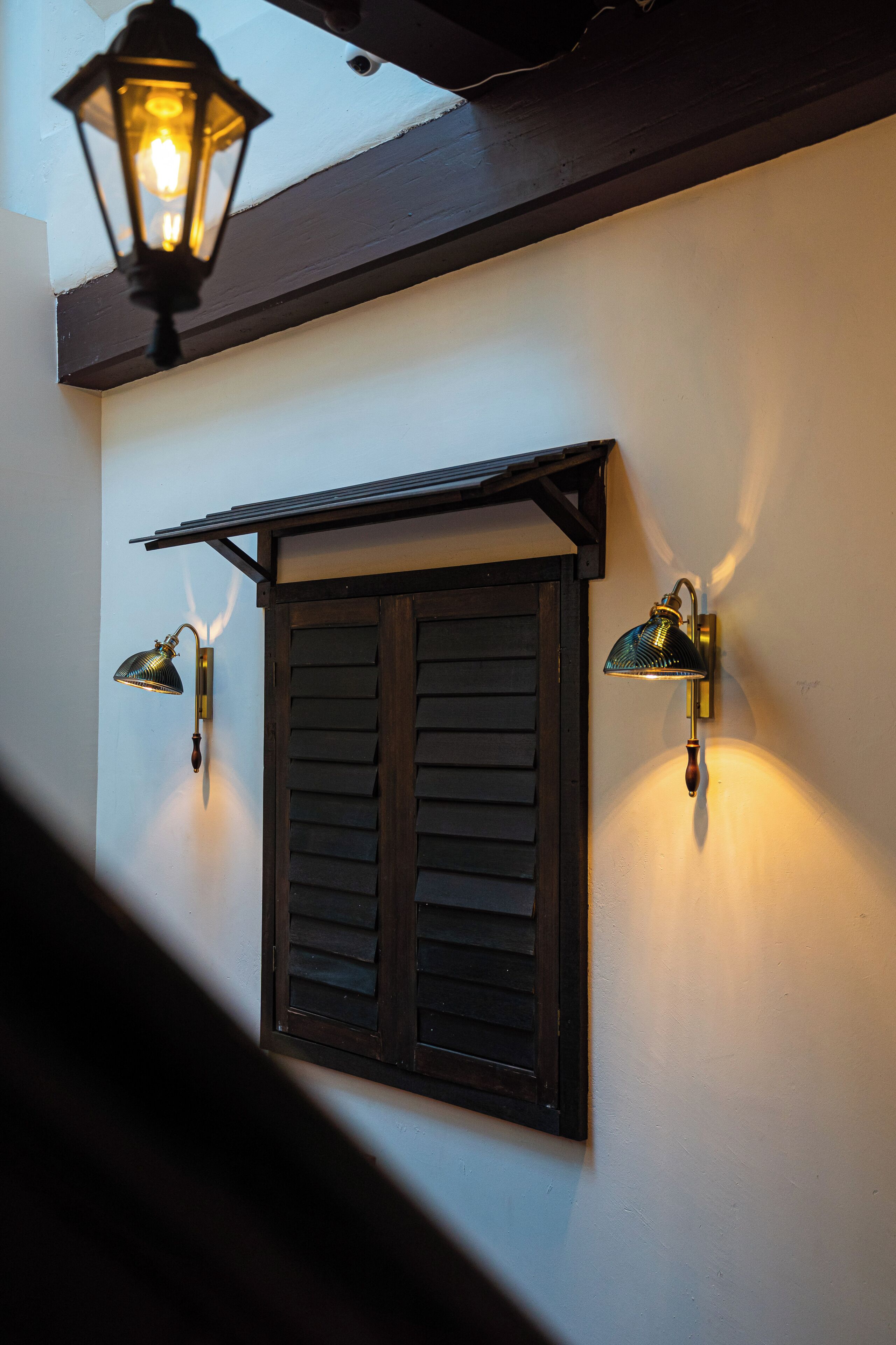 A building exterior with a wooden shuttered window and two wall-mounted lantern-style lights.