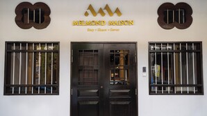 L’entrée d’un hôtel, avec une porte en bois sombre, deux fenêtres grillagées et un logo au-dessus de la porte.