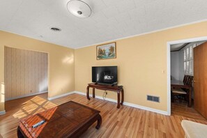 A living room with a wooden floor, a television on a stand, and a painting on the wall. - The Newberry Opera House (Newberry)