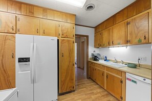 A kitchen with wooden cabinets, a white refrigerator, a sink, and a dishwasher. - The Newberry Opera House (Newberry)