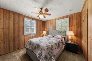 A bedroom with wooden paneling, a tufted headboard bed, two bedside lamps, and a ceiling fan. - The Newberry Opera House (Newberry)