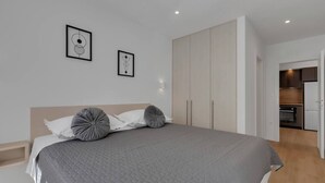 Ein modernes Schlafzimmer mit einem großen Bett, einem Kleiderschrank und einer kleinen Küchenzeile im Hintergrund.