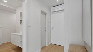 Ein modernes, minimalistisches Zimmer mit weißen Wänden, Holzboden, einem weißen Kleiderschrank, einem weißen Schreibtisch mit Schubladen und einem beigen Kissen.