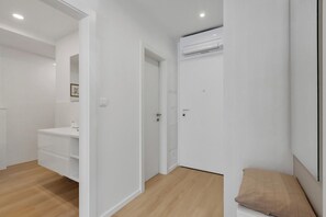 A modern, minimalist room with white walls, a wooden floor, a white wardrobe, a white desk with drawers, and a beige cushion. - Apartment Roza, a beautiful new apartment with parking (Makarska)