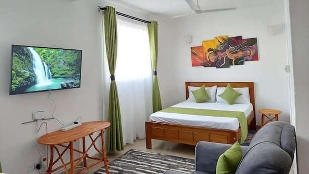 Une chambre à coucher avec un lit, une télévision, un ventilateur de plafond et des œuvres d’art accrochées au mur.