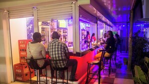 Un espace bar avec des tabourets et un comptoir, entouré d’étagères remplies de bouteilles et d’un réfrigérateur à boissons, notamment des Coca-Cola.