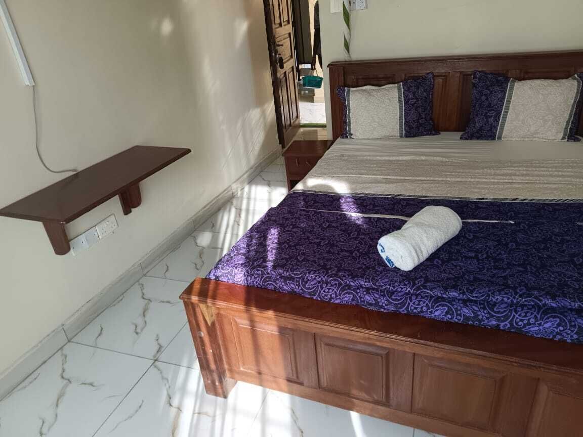 A bedroom with a wooden bed, a nightstand, a wall-mounted shelf, and a tiled floor.