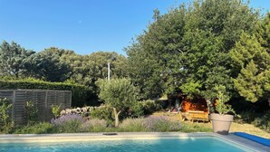 A swimming pool with a wooden deck, surrounded by a garden with various plants and a wooden fence. - Country house surrounded by lavender fields and vineyards (Grignan)