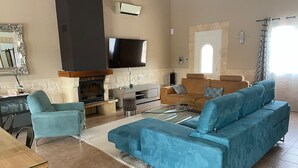 A spacious living room with a large sofa, a fireplace, a television, and a stone wall. - Country house surrounded by lavender fields and vineyards (Grignan)