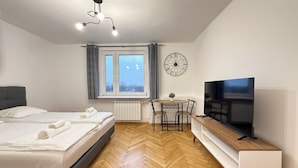 Une chambre d’hôtel moderne dotée d’un grand lit, d’un bureau avec une télévision, d’une petite table avec des chaises et d’une grande fenêtre avec des rideaux.