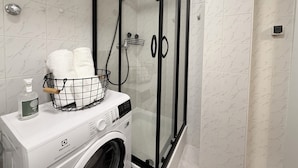 Une salle de bain compacte avec une douche à parois de verre, un lave-linge et un porte-serviettes avec des serviettes.