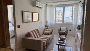 A modern living room with a sofa, a small table, and a view of the city through large windows. - Ipanema with SEA VIEW and total comfort (Rio de Janeiro)